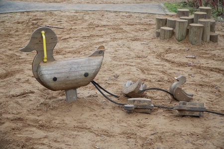 Minimalist Scandinavian children playground sandpit featuring handmade wooden duck with yellow beak followed by three small ducklings on ropes all crafted from natural untreated timber surrounded by log stumpsの写真素材