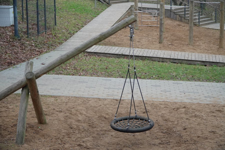 Minimalist Scandinavian-style wooden swing set made from natural logs with two round nest swings hanging on ropes in quiet autumn or spring park playground crafted from eco-friendly untreated timberの写真素材