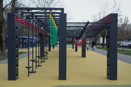 modern urban obstacle course with hanging rings climbing nets monkey bars and rope obstacles on soft rubber surface in public park with people trainingの写真素材