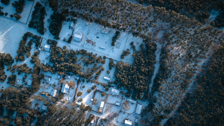 Aerial view of Nowy Lubiel, Poland, snow covers roofs and roads in a loose grid among pine stands. Long tree shadows suggest low sun, cabins and forest lanes appear.の写真素材