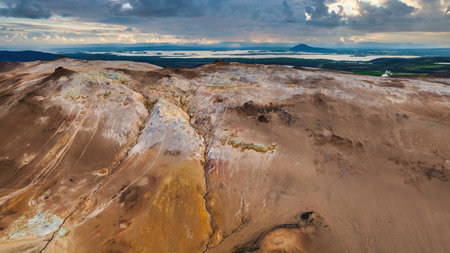 Aerial view shows sulfur ridges and steaming vents at Namafjall Hverir near Lake Myvatn, with Hverfjall and island dotted waters under late day clouds.の写真素材