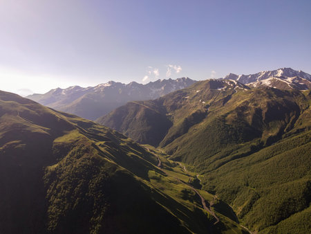 Aerial view shows the Greater Caucasus in Georgia with snow peaks, grassy slopes, a narrow river,...