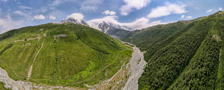 Aerial view of Ushba and Mestia range in Georgia near Svaneti. A braided pale gray riverbed winds...