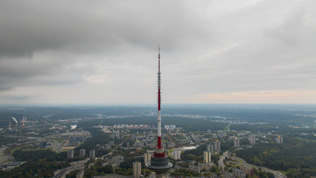 The Vilnius Television Tower rises above a mix of urban buildings, winding roads, and forested areas under an overcast sky in Vilnius, Lithuania.の写真素材