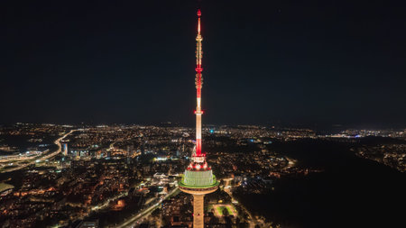 The Vilnius Tower stands lit with red and green lights against a dark sky, surrounded by the city's urban lights and roadways at night.の写真素材