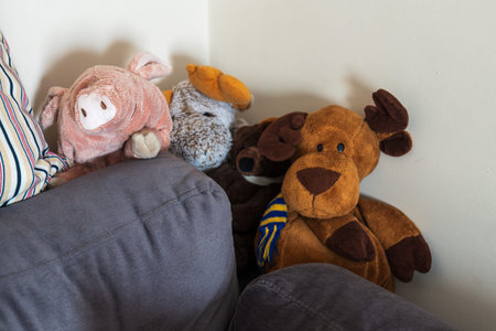 Close up of a pink piglet, a gray donkey, and a brown moose on gray sofa cushions in an apartment, softly lit and warm in tone.の写真素材