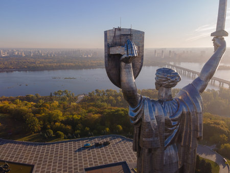 The Motherland Monument in Kyiv, Ukraine, stands tall with a sword and shield. The Dnipro River and cityscape are visible.の写真素材