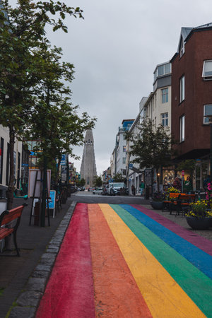 A vibrant street in Reykjavik, Iceland, with a rainbow painted path, colorful buildings, and Hallgrimskirkja church visible in the background.の写真素材