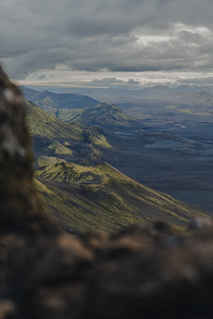 A dramatic Icelandic landscape with volcanic plains, mossy slopes, and rolling green hills under an overcast sky, showcasing rugged terrain.の写真素材