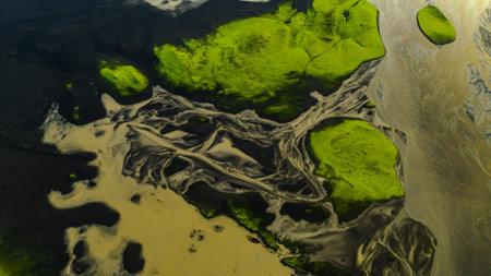 Aerial image of braided light colored rivers flowing through dark volcanic terrain, surrounded by vibrant green moss in Iceland's natural landscape.の写真素材
