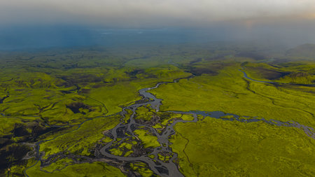 Aerial perspective of Iceland's green moss covered volcanic terrain with winding rivers and streams, set against a misty horizon and dramatic scenery.の写真素材