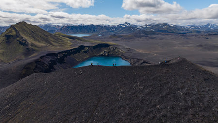 Dramatic aerial view of a vivid blue volcanic crater lake in Iceland, surrounded by dark terrain, snow capped mountains, and a distant second lake.の写真素材