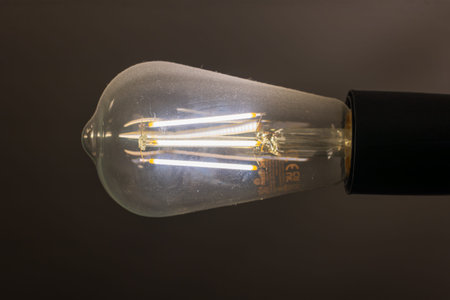 A glowing LED filament bulb with teardrop glass and black socket is set against a dark backdrop in...