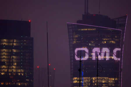 Night cityscape in Warsaw, Poland shows Warsaw Spire and a second tower in heavy haze, windows...