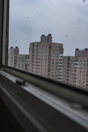 A slightly ajar window frames Soviet era panel apartment blocks, beige facades with pink and orange...
