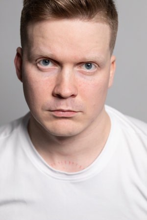 Professional headshot of a middle-aged man with short brown hair wearing a plain white t-shirt...