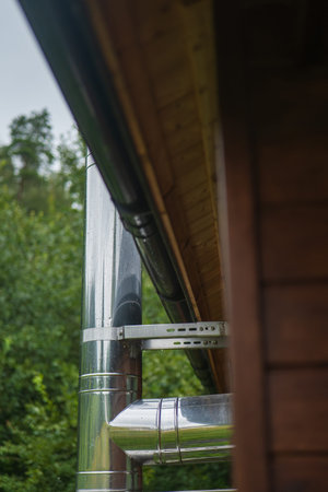 Polished stainless steel chimney and ductwork mount to a wooden cabin as rain droplets bead on...