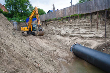 Orange excavator on tracks. The excavator pulls the plastic tube. Excavator produces operation in a trench of sandの写真素材