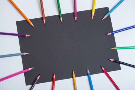 Bright colored pencils lined around the perimeter of the black sheet. Colored pencils on black and...