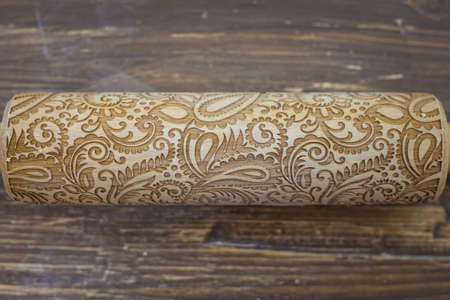 The pattern on the rolling pin. Wooden rolling pin is on the table. Pattern of flowers and leaves on wooden surface for imprint on the dough or clay. Wooden background.の写真素材