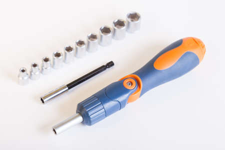Top view of the screwdriver with the adapter. A set of heads and a screwdriver on a light background. Metal adapter for the nut. Screwdriver with blue - orange handle and a set of heads under the nut.の写真素材