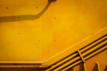 Bright yellow background. Paint smudges on the surface. Painted metal surface. Metal painted yellow. Old painted surface. Pipe hydraulics on the body of the train.の写真素材