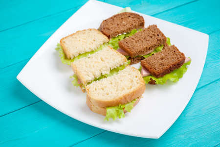 White plate with bruschetta ham and greens is on wood surfaces blue. Food for coffee breaks.