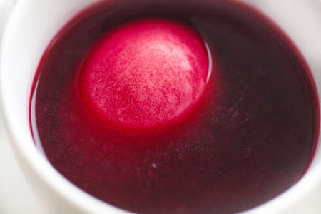 The process of coloring Easter eggs. Eggs are immersed in liquid with paint. White mugs with colored liquid stand on the windowsill. Red spot.の写真素材