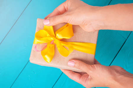 Female hands holding a gift. The girl unpacks the gift. The woman gives you a gift. Yellow bow on the gift. Rotated view with flashの写真素材