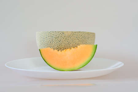Half of a melon and a slice lying on a white plate