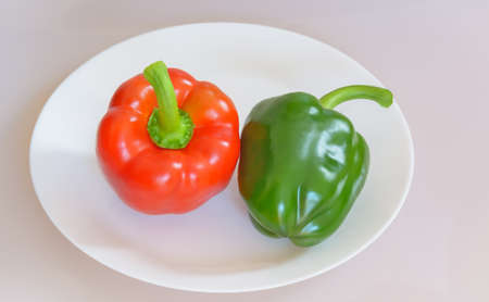 Two sweet peppers, green and red on a white plate