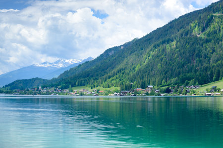 View of the Weissensee lake and a low green mountain with a cloudy sky in a horizontal formatの写真素材