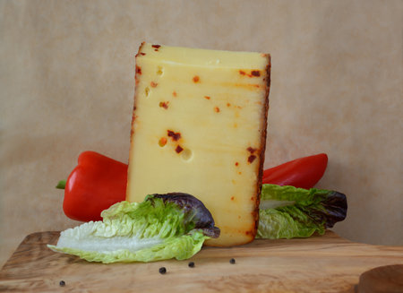 A piece of cheese with red pepper and a pair of green salad leaves on a background of beige parchmentの写真素材