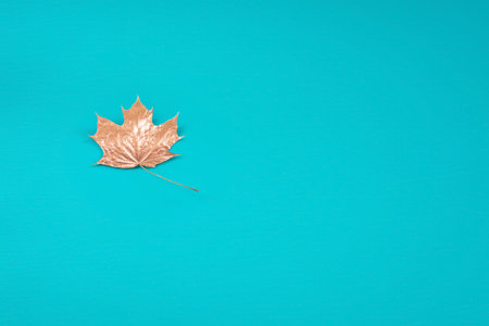 Background with golden maple leaf on turquoise background with copy space in horizontal format