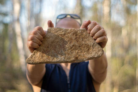 A man holds a stone in his hand, on a blurred background of nature.の写真素材