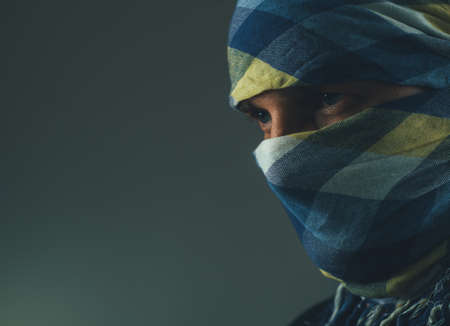 man with a face covered with a colored scarf at duskの写真素材