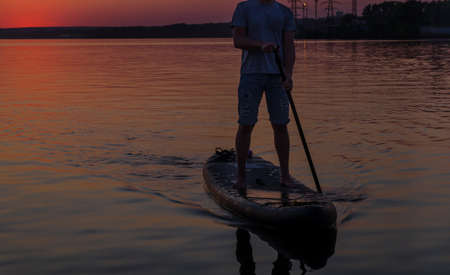 Surfer at sunset rowing with one oar standing on a boardの写真素材