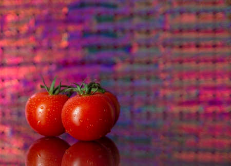 cherry tomatoes on a colored background with reflection in glassの写真素材