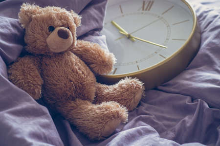 Composition: teddy bear on a gray bed with a wall clock and a metal chainの写真素材