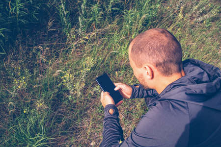 a man sits on the grass with a phone in his hand. View from above