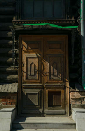 Street paved by cobblestones. Old wooden door with an arc. Light brown facade. Door surrounded by creeper plant.の写真素材