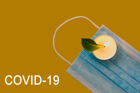 Several blue viral masks on a yellow background with candles on which a green leaf liesの写真素材