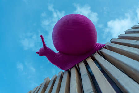 Large pink plastic snail crawling on wooden planks against the skyの写真素材