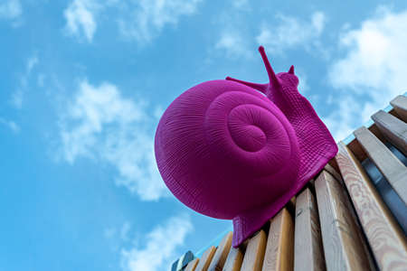 Large pink plastic snail crawling on wooden planks against the skyの写真素材