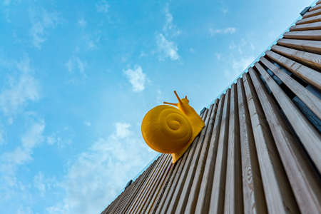 Large yellow plastic snail crawling on wooden planks against the skyの写真素材