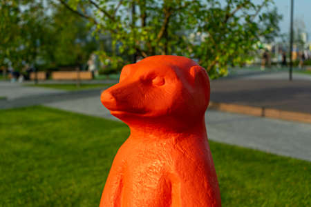 A figure of a meerkat made of colored plastic stands in the park on the grassの写真素材