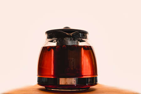hot tea with berries in a glass teapot, on a light background in the dark