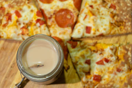 a cup of tea with milk and a tea bag. sliced pizza on a wooden boardの写真素材