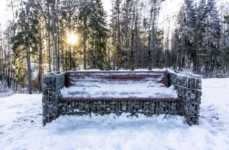 Unusual bench made of stones and wire.Frosty winter morning. Bright sun rays make their way through the trees.の写真素材