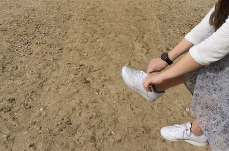 A girl shakes out sand from white sneakers. Large free space. Remove everything that interferes with...